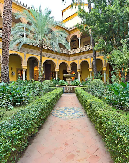 Courtyard of Palacio de las Dueñas in Seville with arches and lush greenery.