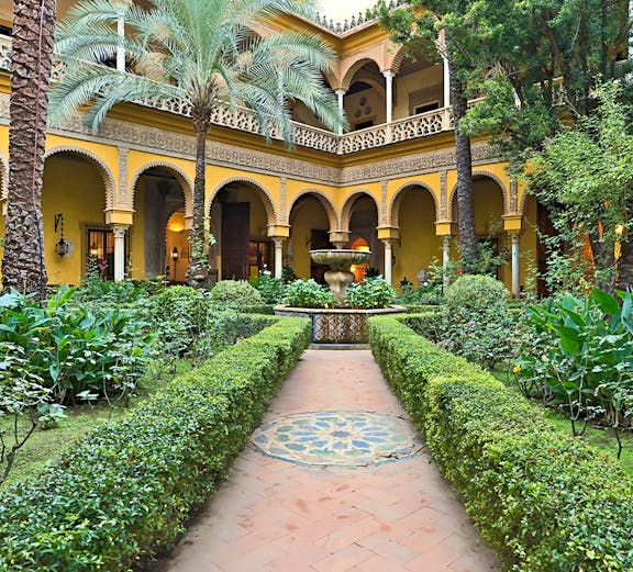 Courtyard of Palacio de las Dueñas in Seville with arches and lush greenery.