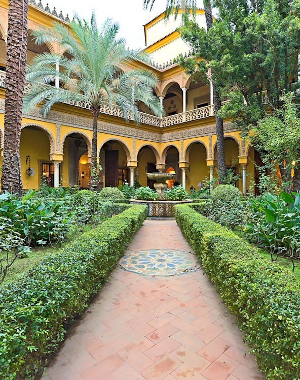 Courtyard of Palacio de las Dueñas in Seville with arches and lush greenery.