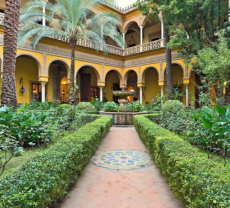 Palacio de las Dueñas courtyard with arches and lush gardens in Seville.