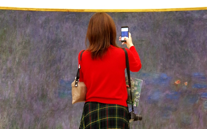 Tourist photographing Monet's Water Lilies at Orangerie Museum, Paris.
