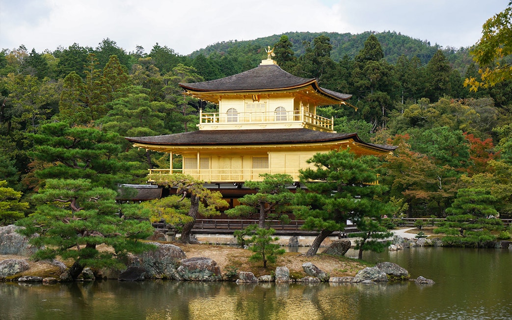 Kinkaku-Ji Temple in Kyoto surrounded by trees and reflecting in a pond.