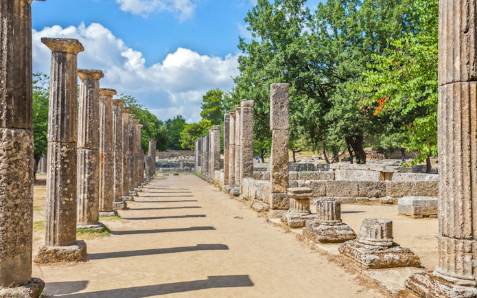 Ancient columns of the Palaestra in Olympia, Greece, under a clear summer sky.