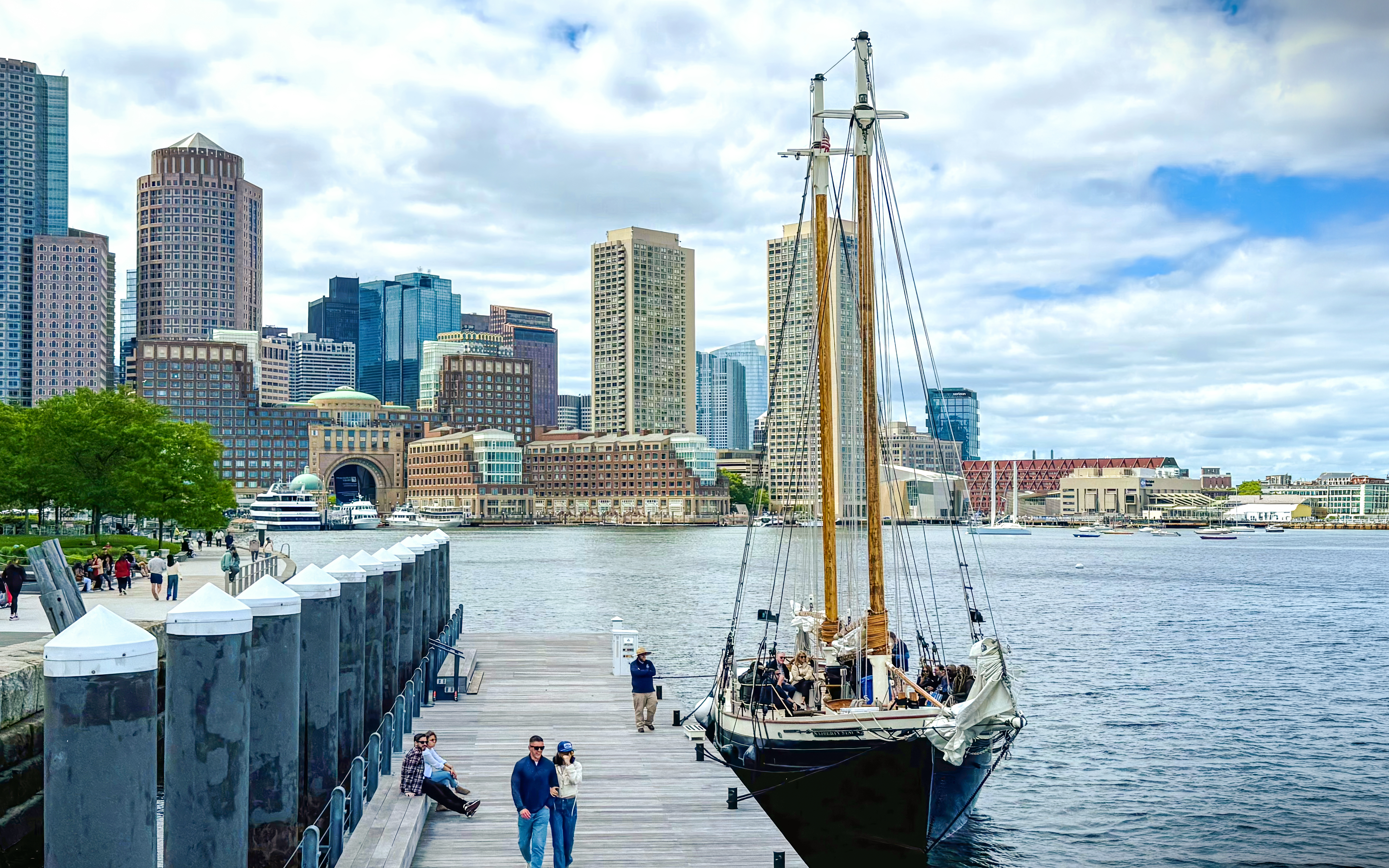 Boston skyline from the harbor with Liberty Fleet tall ship docked in foreground.