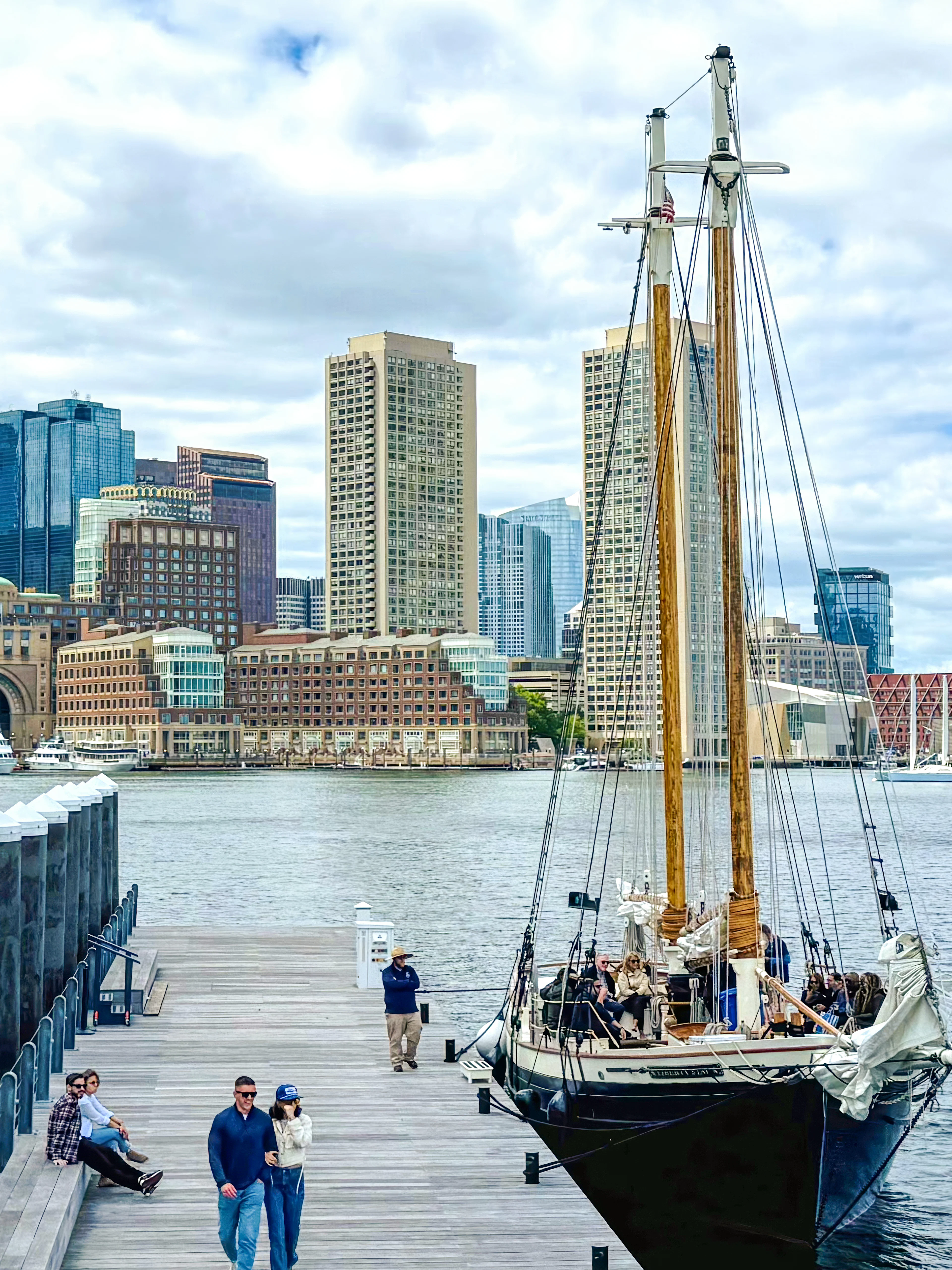 Boston skyline from the harbor with Liberty Fleet tall ship docked in foreground.