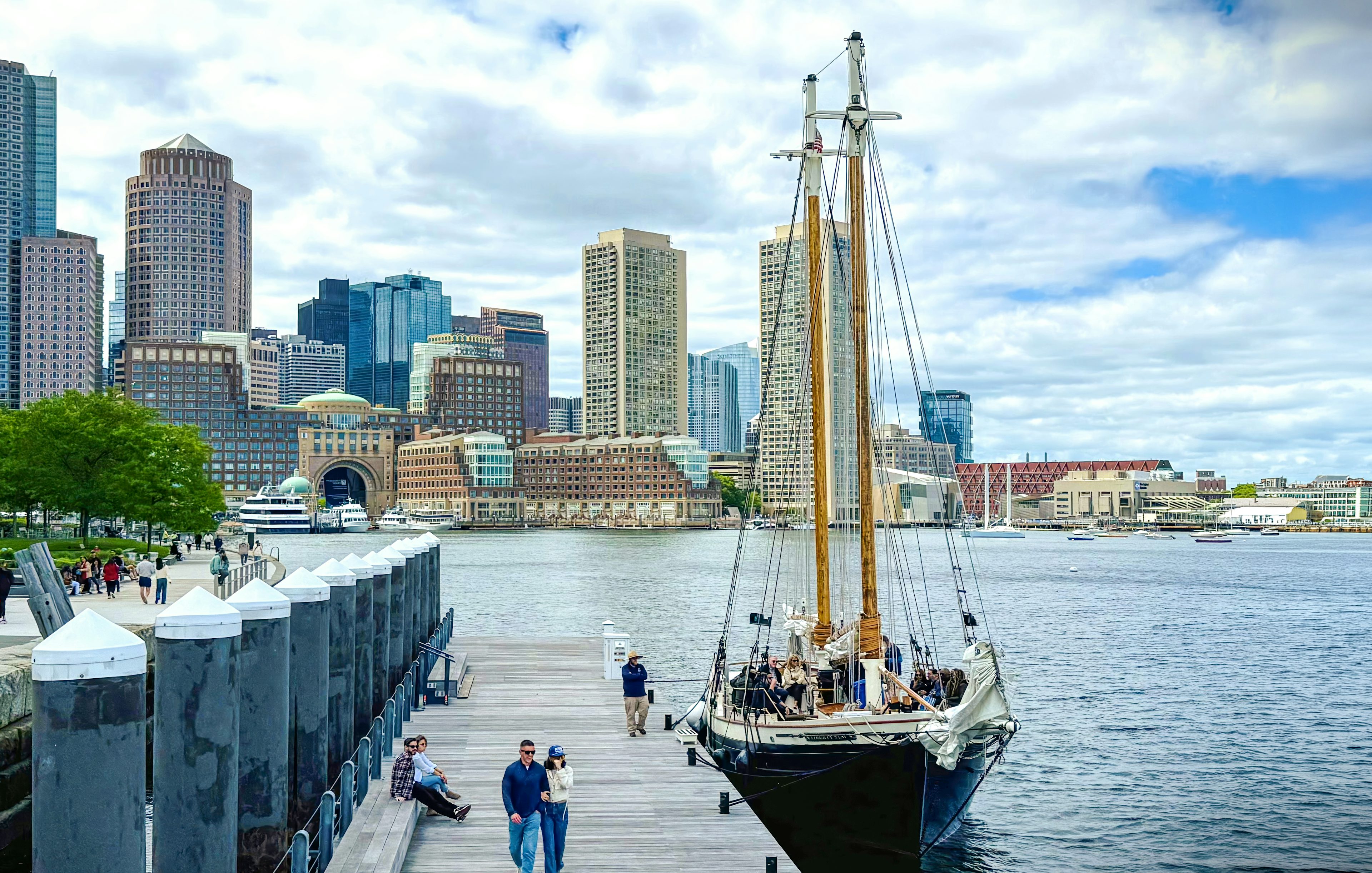 Boston skyline from the harbor with Liberty Fleet tall ship docked in foreground.