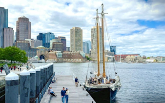 Boston skyline from the harbor with Liberty Fleet tall ship docked in foreground.