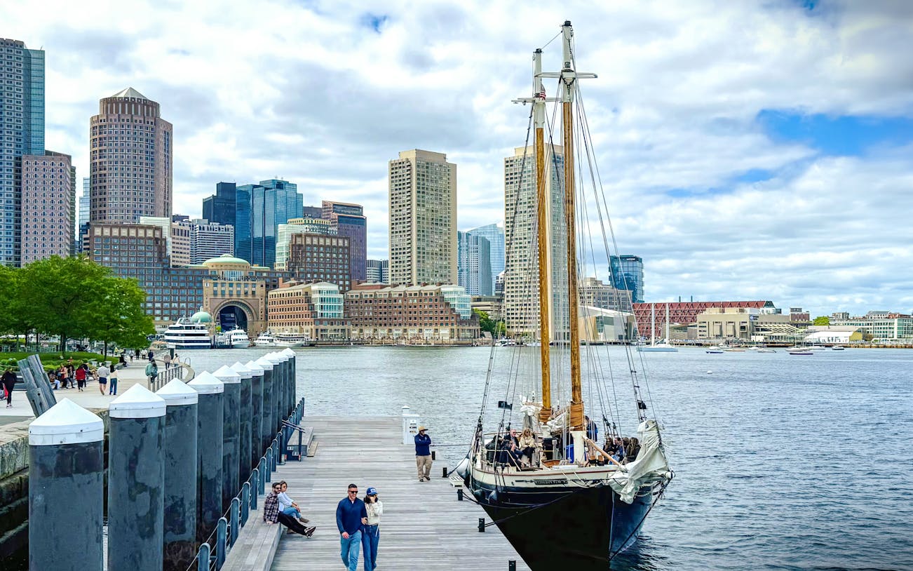 Boston skyline from the harbor with Liberty Fleet tall ship docked in foreground.
