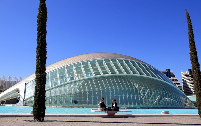 Hemisfèric building in Valencia with two people sitting by the reflecting pool.
