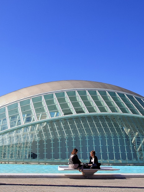 Hemisfèric building in Valencia with two people sitting by the reflecting pool.