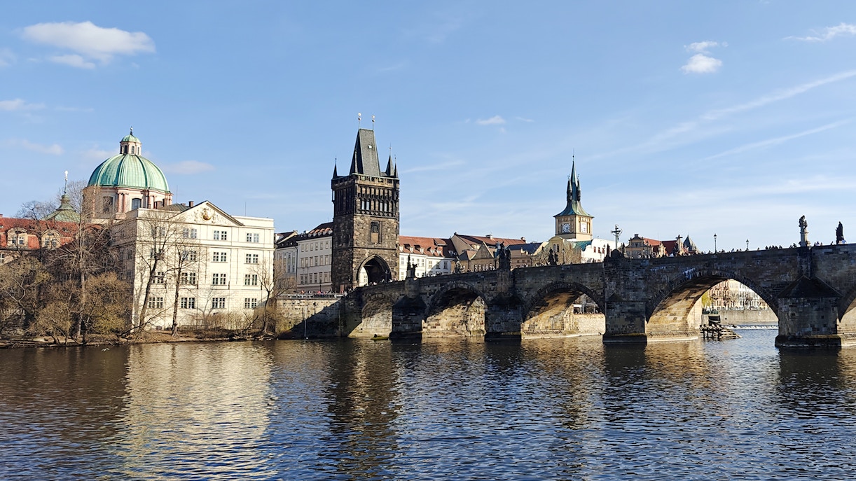 Charles Bridge spanning the Vltava River in Prague with historic buildings in the background.