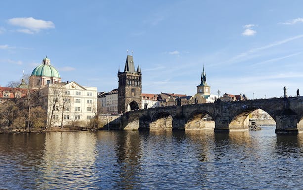 Charles Bridge spanning the Vltava River in Prague with historic buildings in the background.
