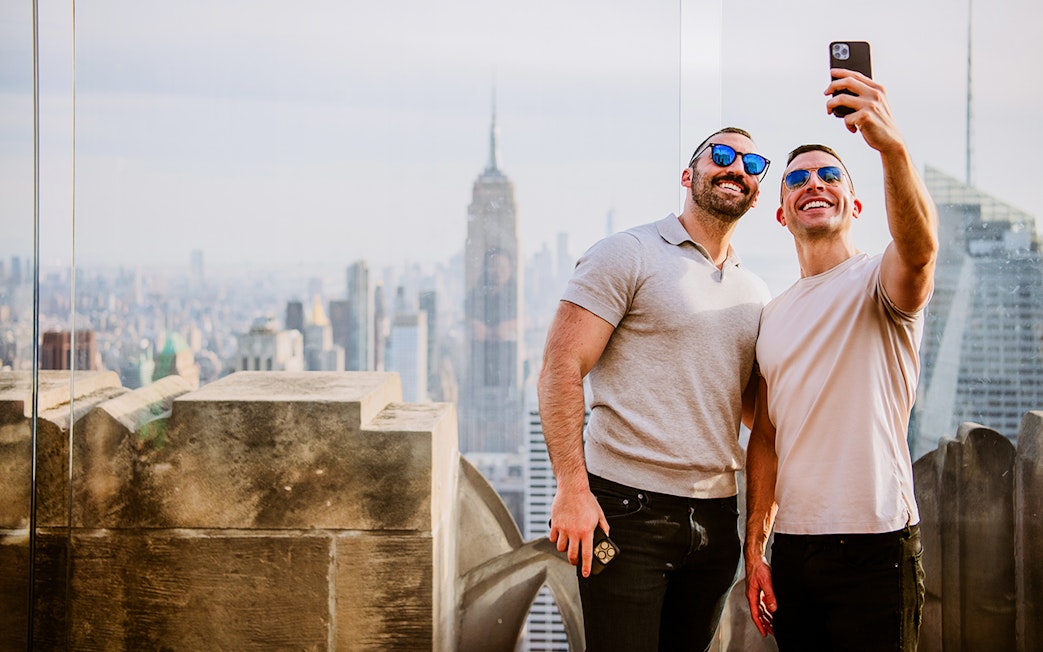 Two men taking a selfie with New York City skyline and Empire State Building from Top of the Rock.
