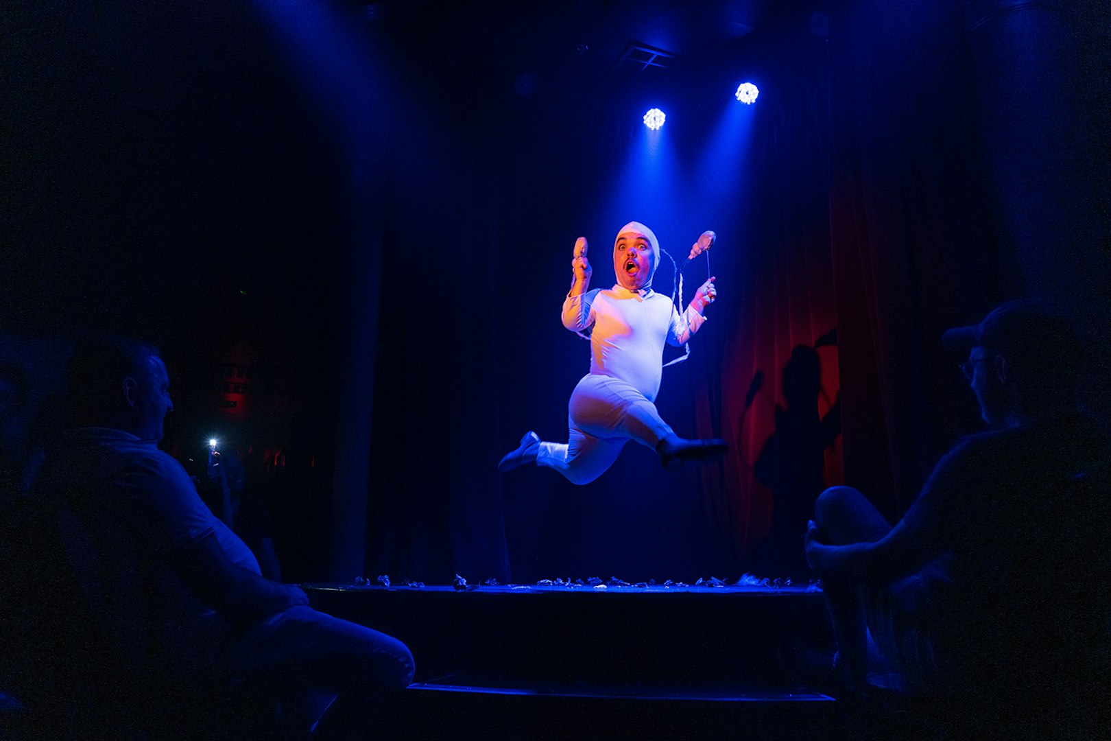 Performer in white costume jumping on stage at Miss Behaves: Maverick's Variety Show.
