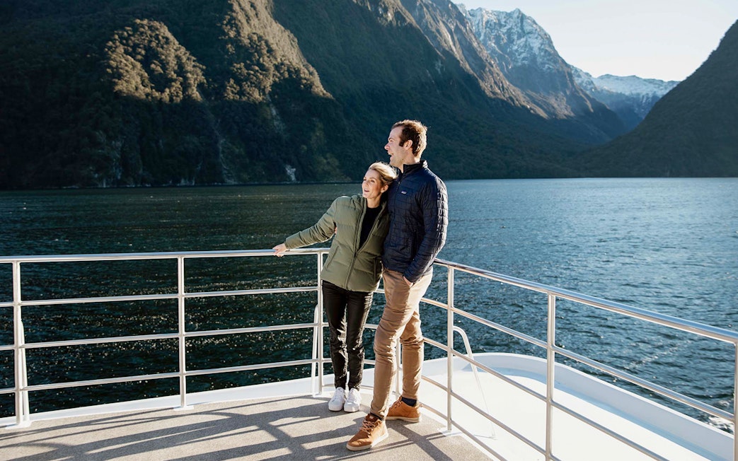 Couple enjoying Milford Sound views from a cruise deck, surrounded by mountains and water.