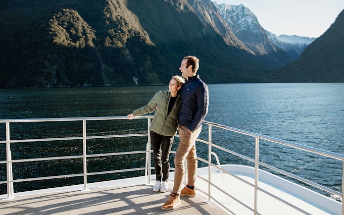 Couple enjoying Milford Sound views from a cruise deck, surrounded by mountains and water.