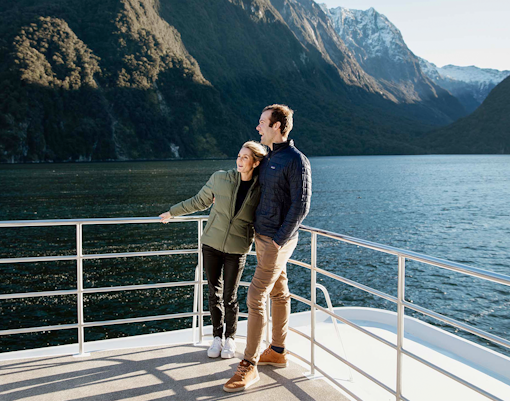 Couple enjoying Milford Sound views from a cruise deck, surrounded by mountains and water.