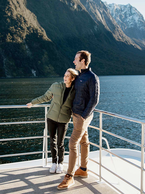 Couple enjoying Milford Sound views from a cruise deck, surrounded by mountains and water.