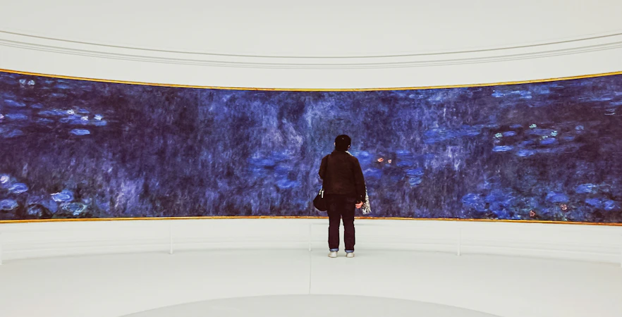 Visitor admiring Monet's Water Lilies at Orangerie Museum exhibition.