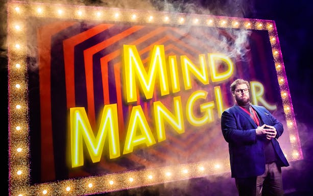 Performer on stage with "Mind Mangler" sign, part of the Tragic Circle show.