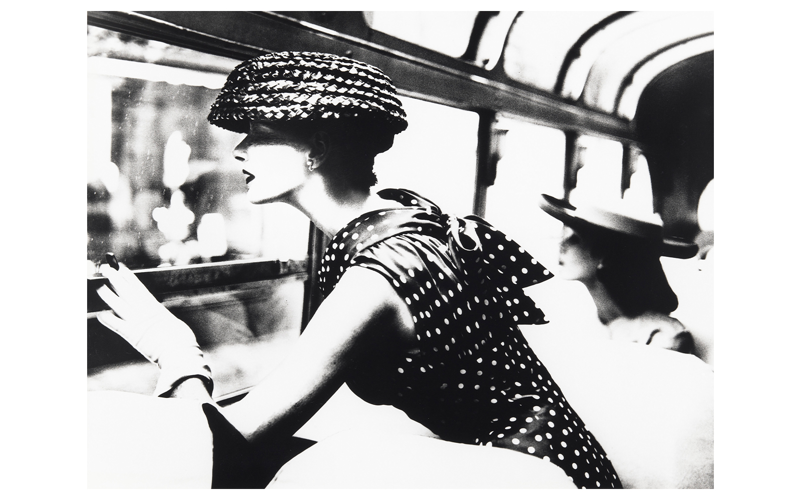 Woman in polka dot dress and hat looking out a window, part of the National Gallery of Victoria exhibition.
