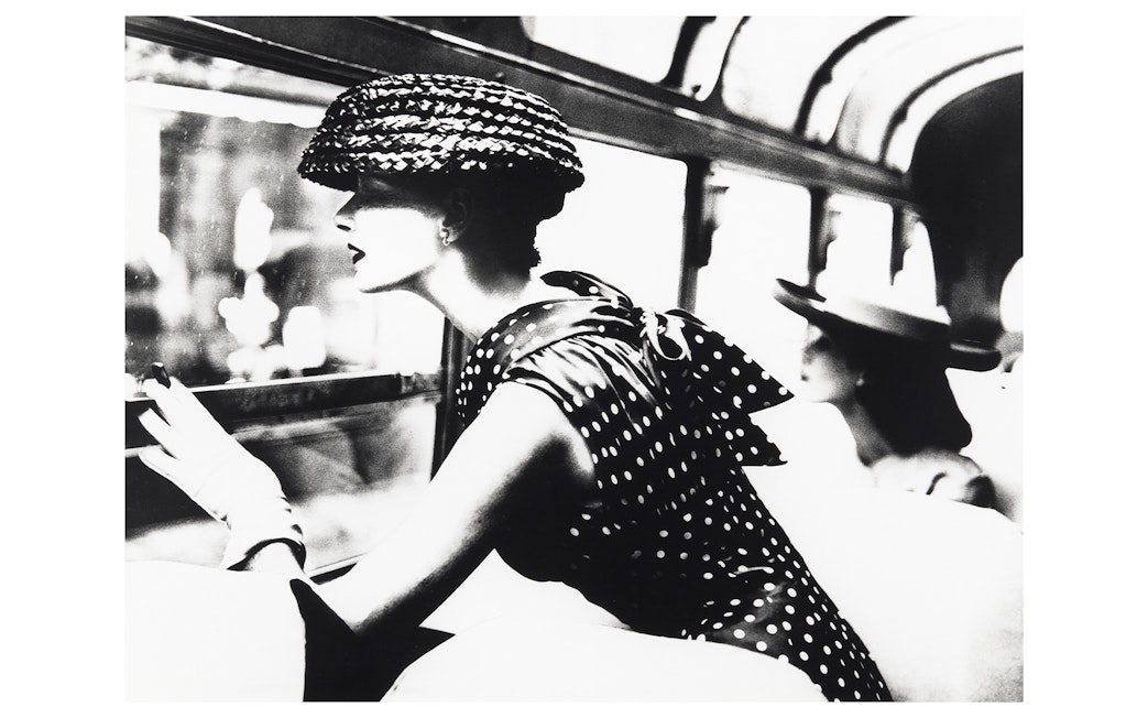 Woman in polka dot dress and hat looking out a window, part of the National Gallery of Victoria exhibition.