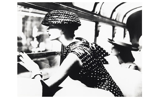 Woman in polka dot dress and hat looking out a window, part of the National Gallery of Victoria exhibition.