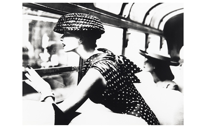 Woman in polka dot dress and hat looking out a window, part of the National Gallery of Victoria exhibition.