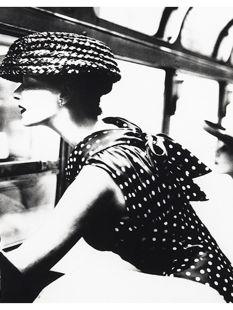 Woman in polka dot dress and hat looking out a window, part of the National Gallery of Victoria exhibition.