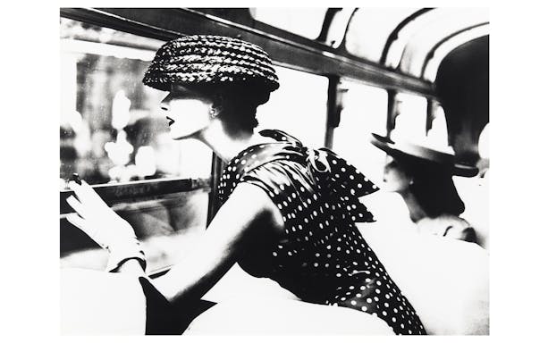 Woman in polka dot dress and hat looking out a window, part of the National Gallery of Victoria exhibition.
