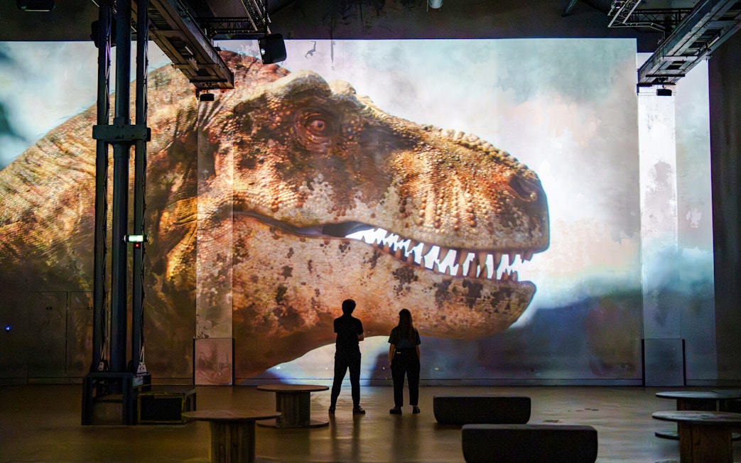 Visitors viewing a large dinosaur projection at Prehistoric Planet exhibition, Atelier des Lumières.