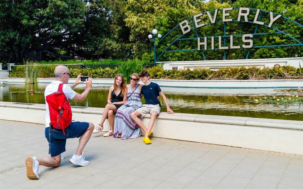 Man photographing family at Beverly Hills Sign, Beverly Gardens Park, California.