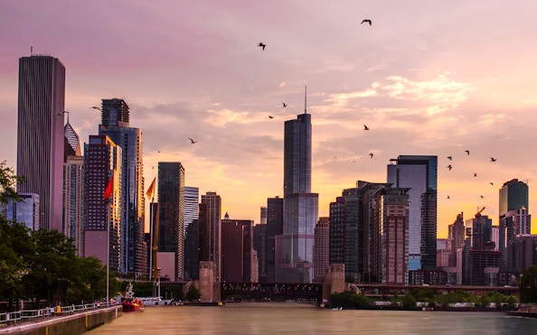 Chicago skyline at sunset with skyscrapers and birds over the river.