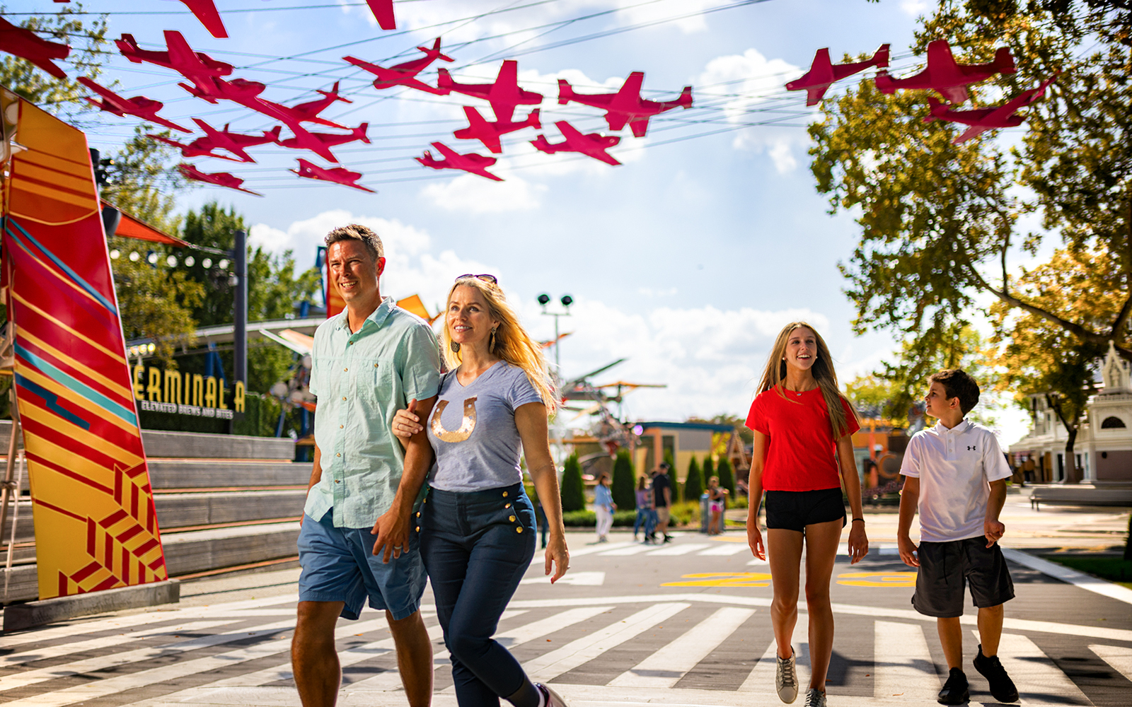 Visitors walking under red airplane decorations at Aeronautica Landing, Six Flags Carowinds.