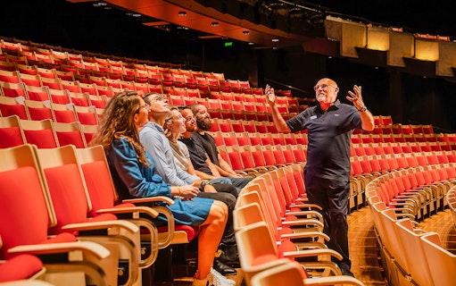 Tour guide explaining to visitors inside Joan Sutherland Theatre at Sydney Opera House.