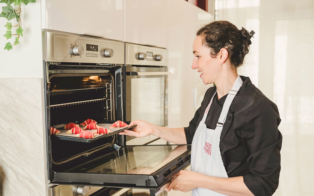 Baker placing croissants in oven during Paris croissant-making workshop.