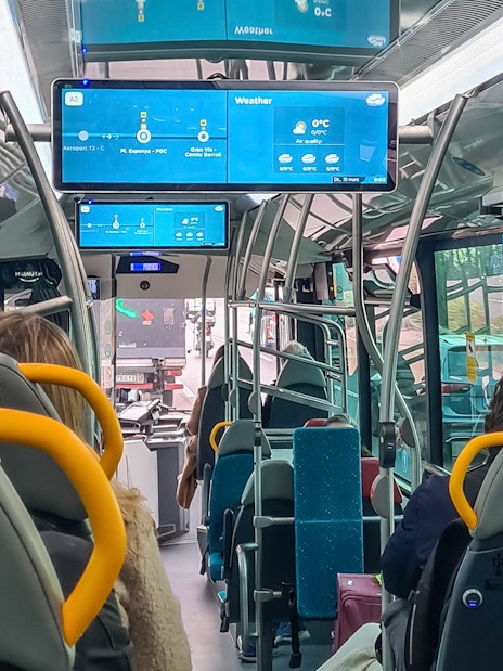 Barcelona Aerobus interior with passengers seated and digital screens displaying route information.