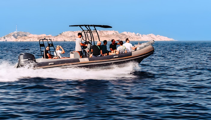 Boat tour with passengers near rocky coastline in Marseille.