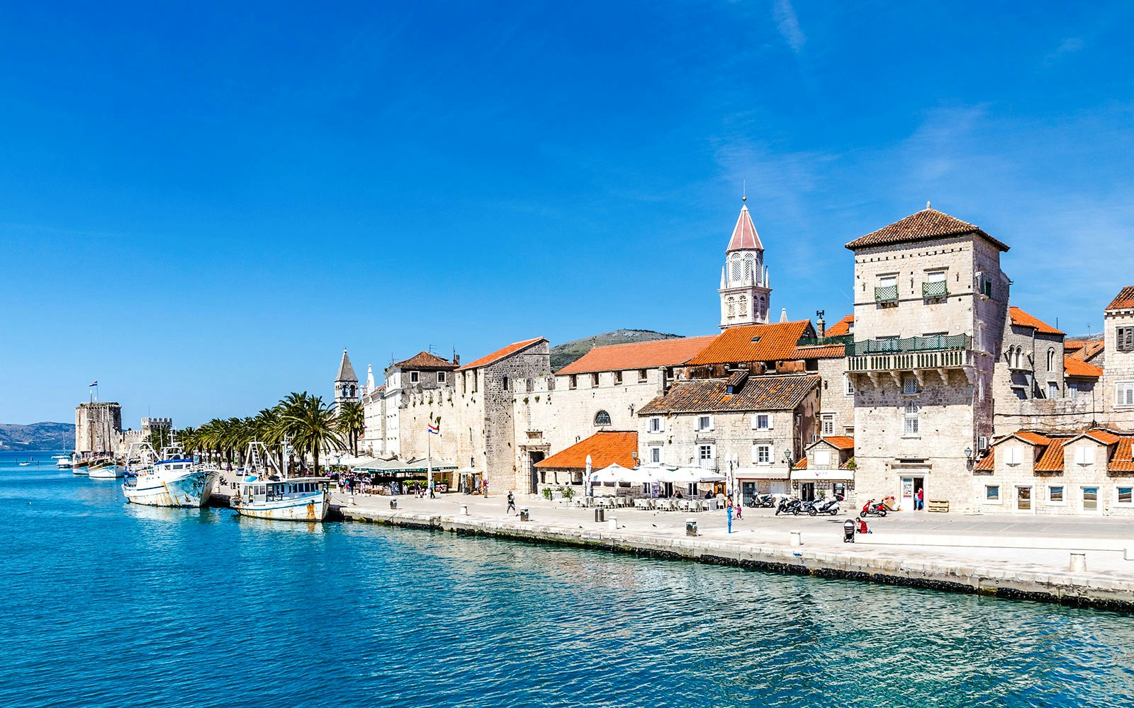 Seafront promenade with historic fortress and boats in Trogir, Croatia.