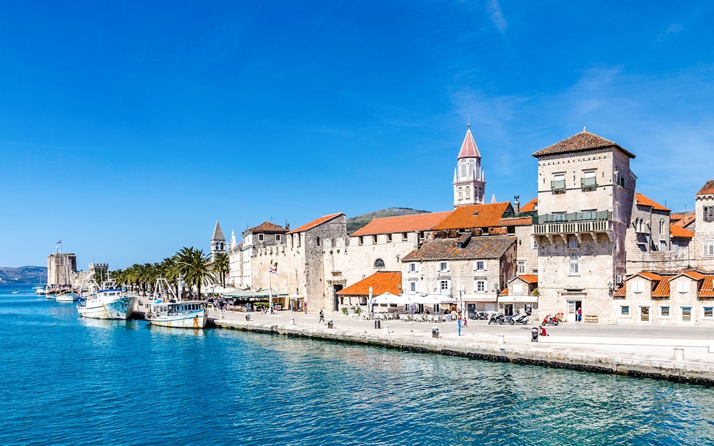 Seafront promenade with historic fortress and boats in Trogir, Croatia.