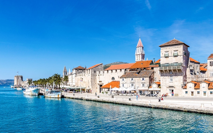 Seafront promenade with historic fortress and boats in Trogir, Croatia.