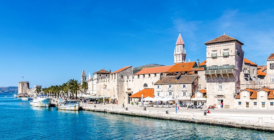 Seafront promenade with historic fortress and boats in Trogir, Croatia.