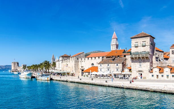 Seafront promenade with historic fortress and boats in Trogir, Croatia.