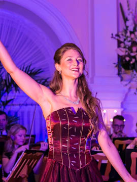 Opera singer performing at Vienna State Opera with orchestra in background.