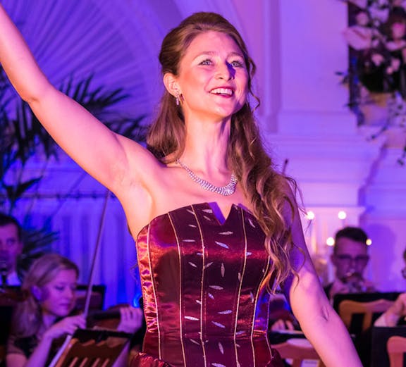Opera singer performing at Vienna State Opera with orchestra in background.