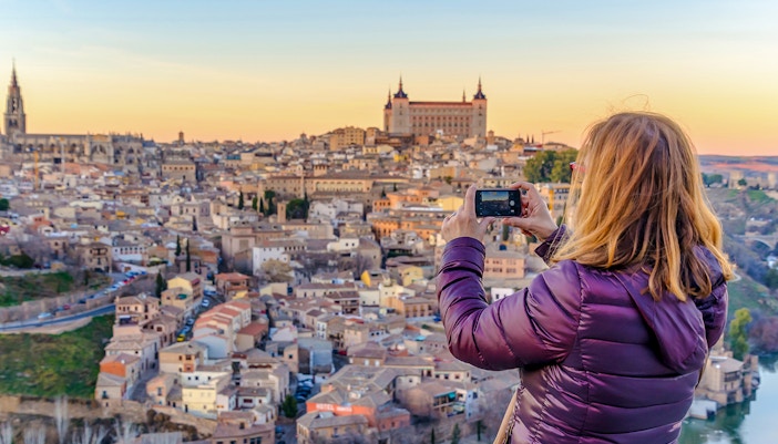 Woman capturing Toledo skyline from Mirador del Valle viewpoint during day trip.