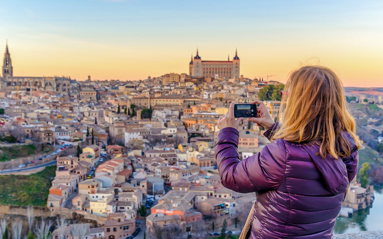 Woman capturing Toledo city skyline from Mirador del Valle viewpoint.