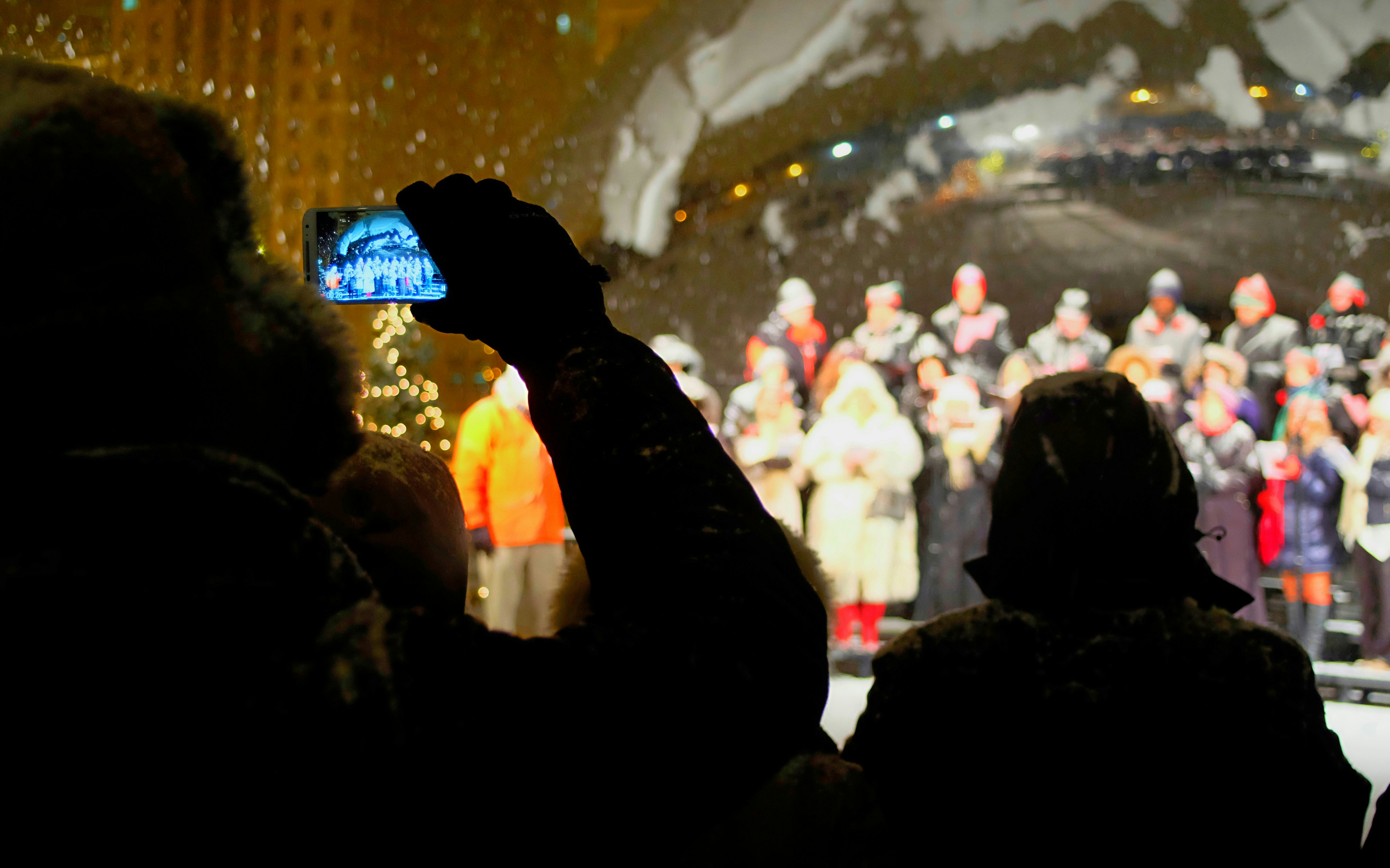 Crowd watching choir perform on snowy winter night.