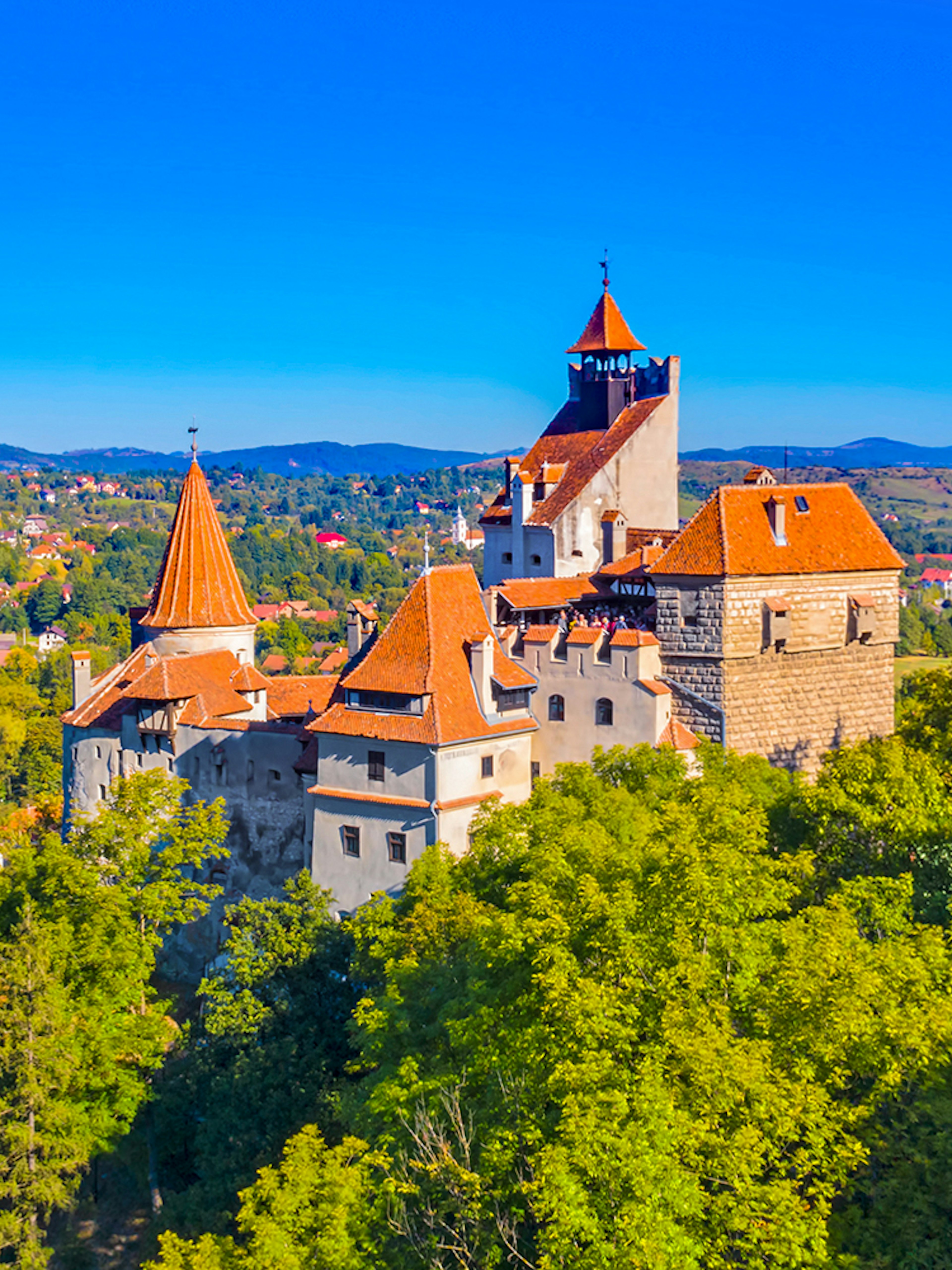 Bran Castle in Romania surrounded by lush greenery and distant hills.