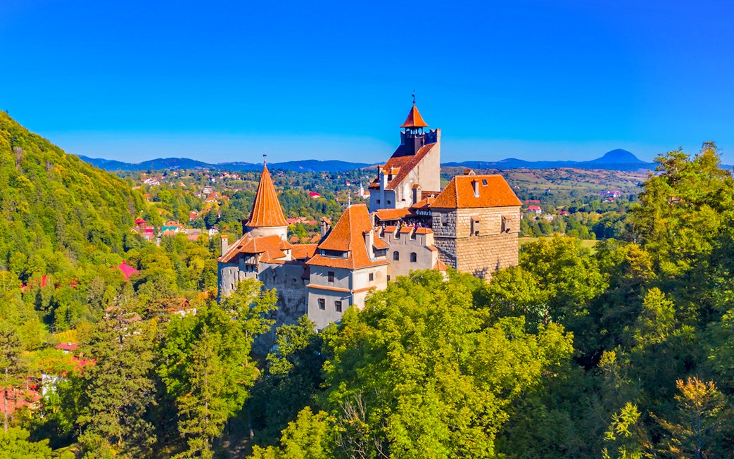 Bran Castle in Romania surrounded by lush greenery and distant hills.